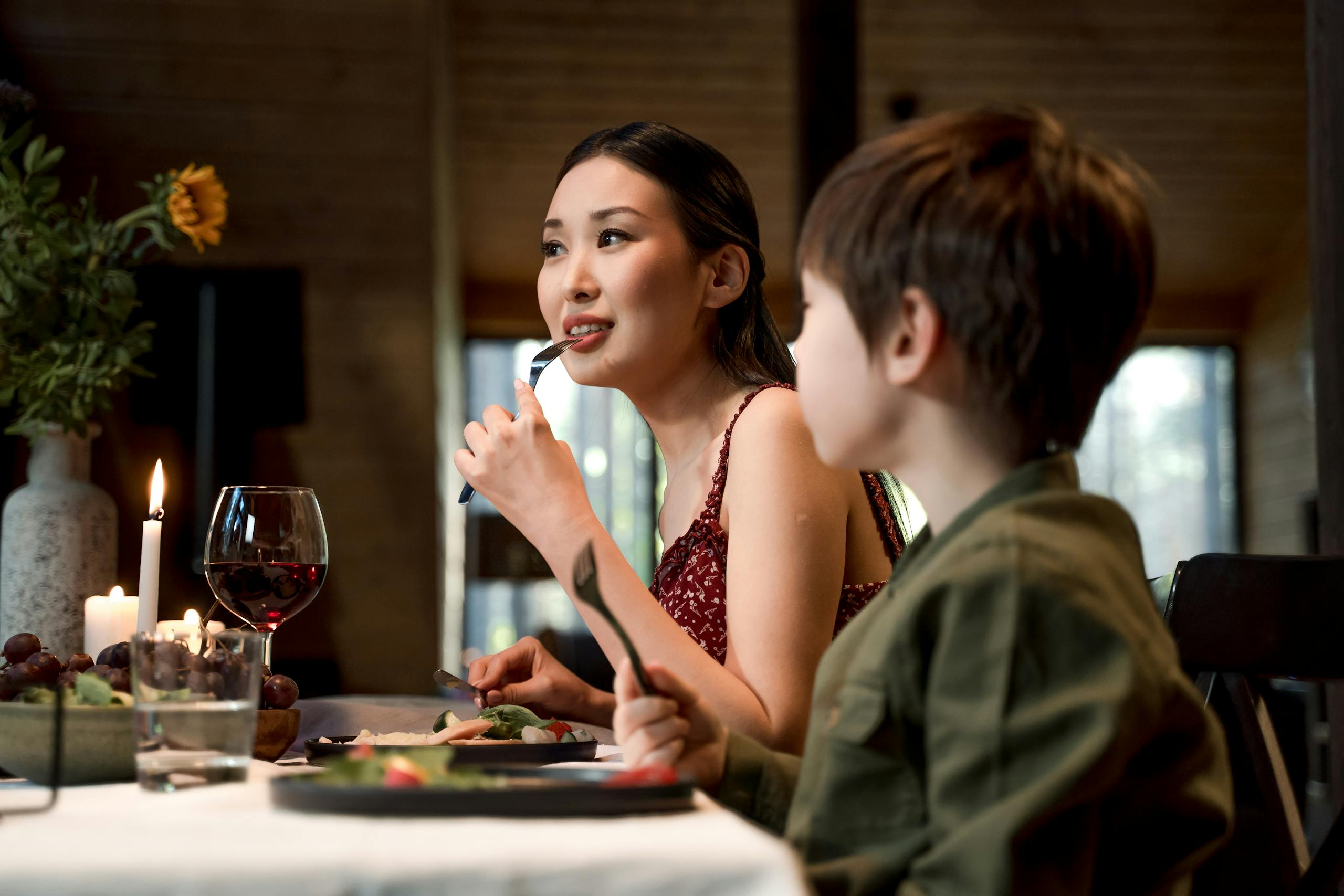 A mother and son share a warm dinner together indoors, surrounded by a cozy atmosphere and candlelight.