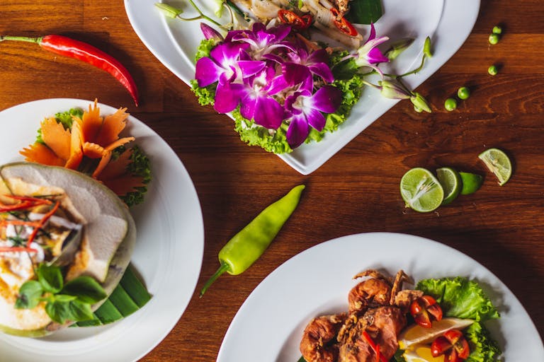 Beautifully presented Thai dishes with vibrant orchids on a wooden table, showcasing diverse flavors.